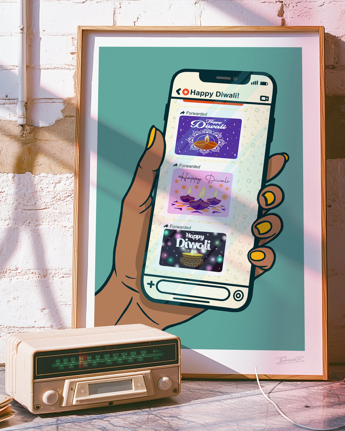 A framed art print leaning against a pink brick wall, featuring a stylized illustration of a hand holding a smartphone with Diwali-themed app screens. A vintage cream-colored radio sits on the floor in front of the frame.